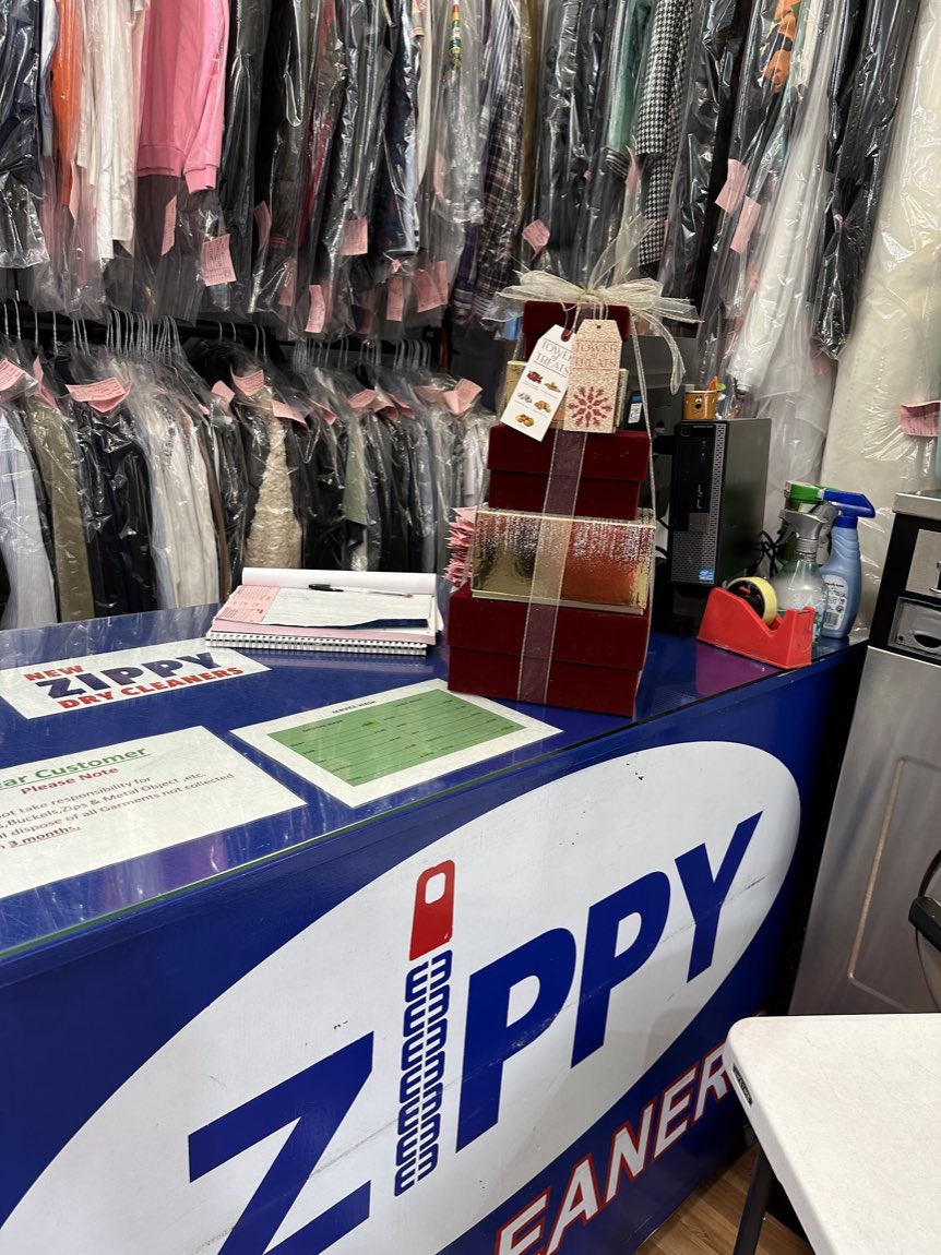 The New Zippy counter with the blue Zippy zip logo, and rows of cleaned garments bagged and ticketed on the rail behind